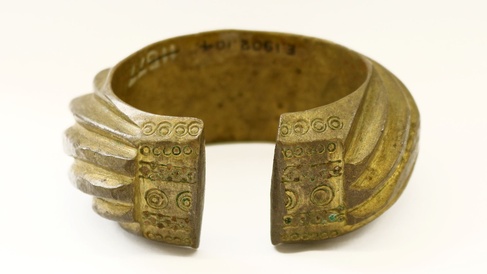 A brass penannular bracelet decorated with heavy slanting bands. 