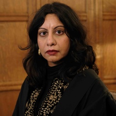 Potrait of Dr Zehra Jumabhoy standing indoors against wood‑panelled walls.
