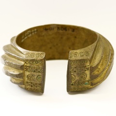 A brass penannular bracelet decorated with heavy slanting bands. 