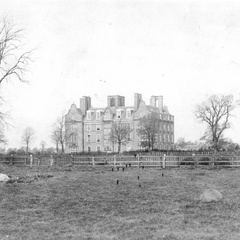 Historic photograph of Newnham College buildings across open grounds.