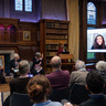 Audience attending a prize-giving ceremony in Girton College’s wood-paneled library, with speakers seated at the front and a large screen for remote participation.