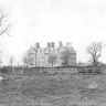 Historic photograph of Newnham College buildings across open grounds.