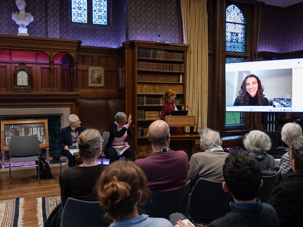 Audience attending a prize-giving ceremony in Girton College’s wood-paneled library, with speakers seated at the front and a large screen for remote participation.