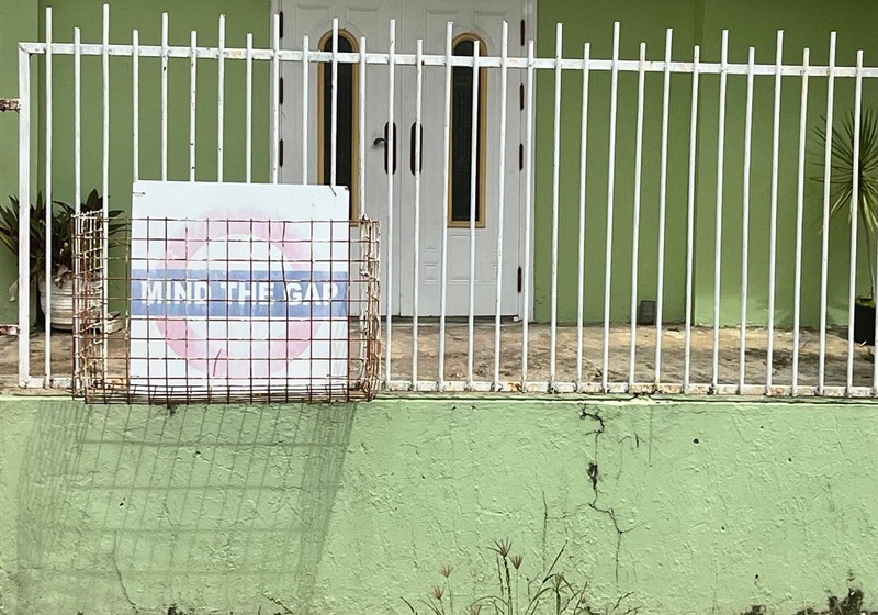 A house in Trinidad and Tobago with a “Mind the Gap” sign on its fence, photographed in a residential street