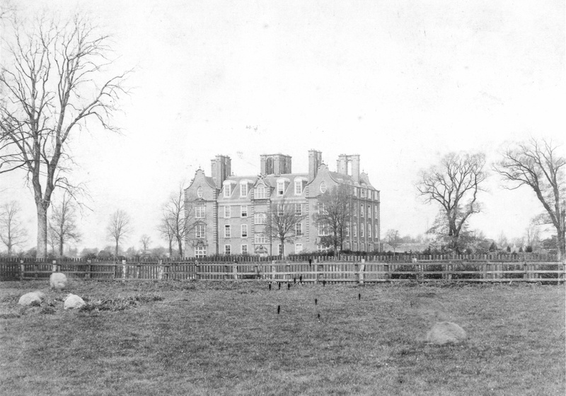Historic photograph of Newnham College buildings across open grounds.